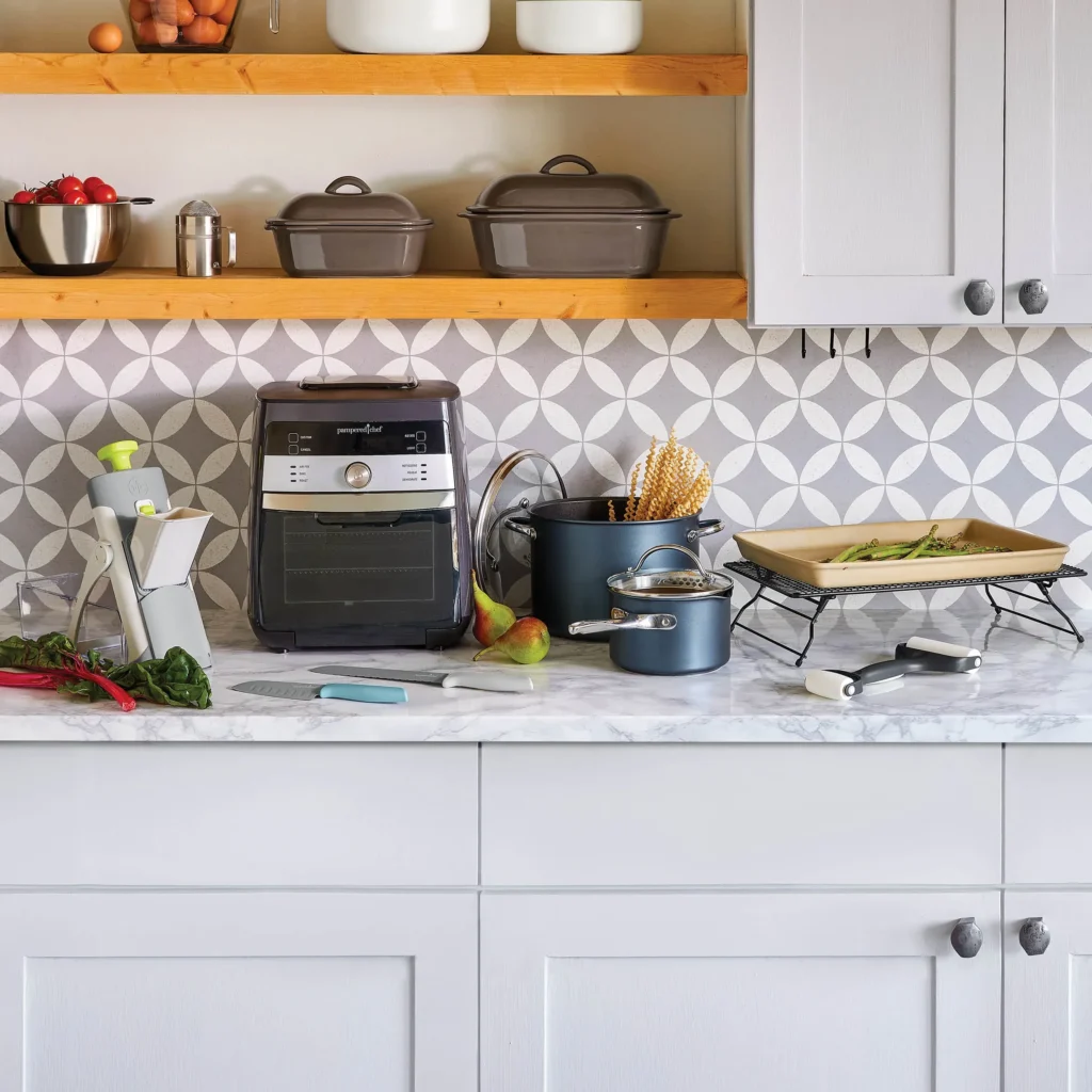 Pampered Chef Produktübersicht – Deluxe Air Fryer, Stoneware, Töpfe und Küchenhelfer auf einer weißen Küchenarbeitsfläche